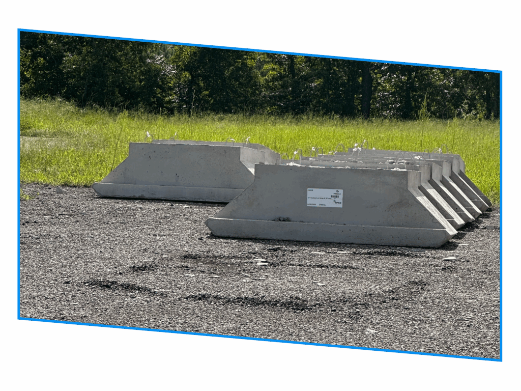Concrete barriers are lined up on gravel, with grass and trees in the background.