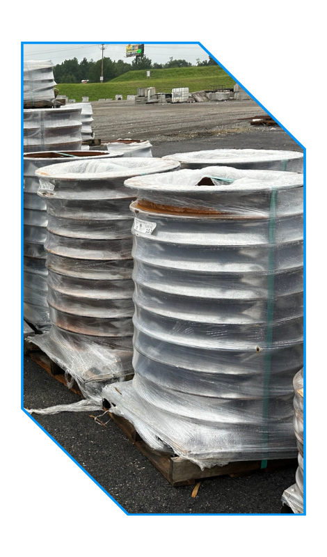 Large metal coils wrapped in plastic and stacked on wooden pallets outdoors.