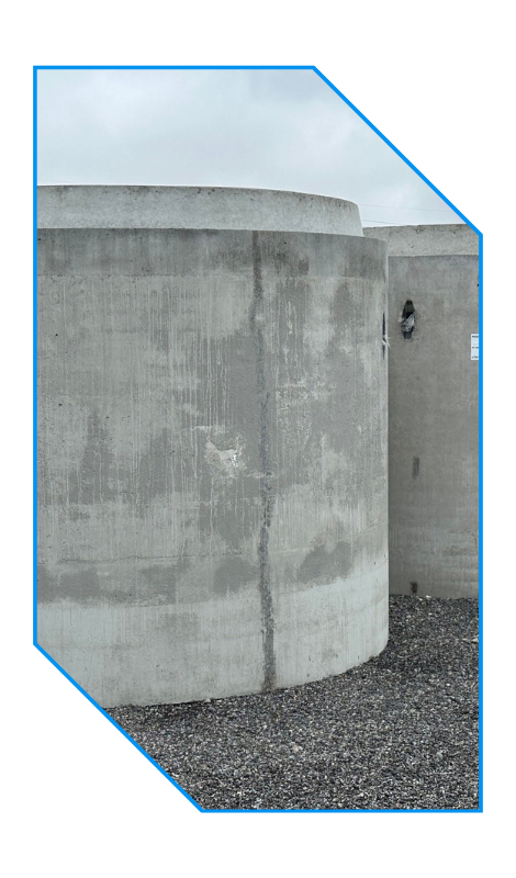 Large round concrete structure on gravel with a cloudy sky in the background.